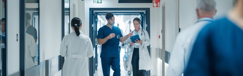 A doctor and a nurse are discussing an upcoming surgery while walking through a busy hospital hallway.