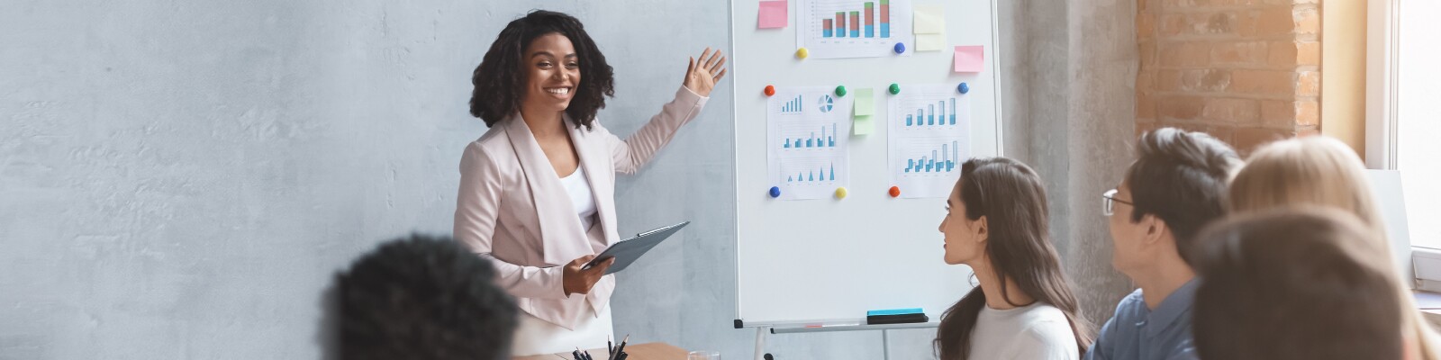 Professional stands next to white board with charts and sticky notes in front of a table of people