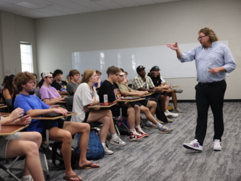 A male KU professor stands in front of the classroom.
