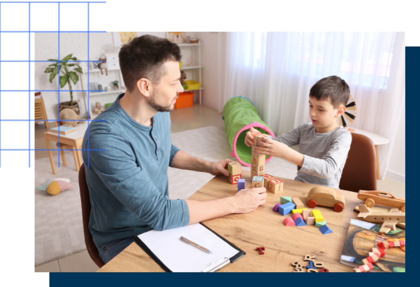A young autistic boy is playing with building blocks while a male teacher observes.