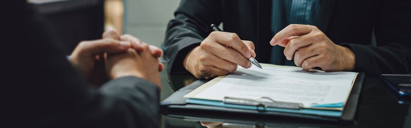 person holding pen and about to sign legal document attached to clipboard