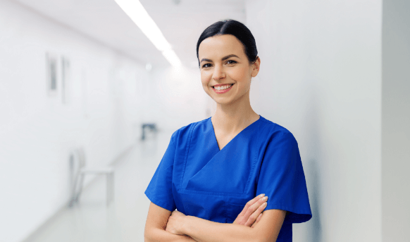 Woman in dark blue scrubs smiling with arms crossed in white hospital hallway