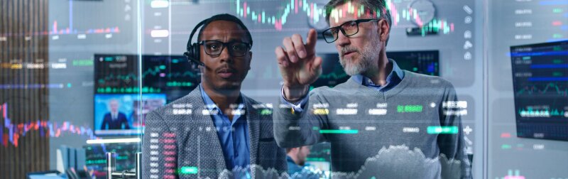 Multiracial financial analysts look on computer generated virtual 3D real-time finance analytics on glass wall.