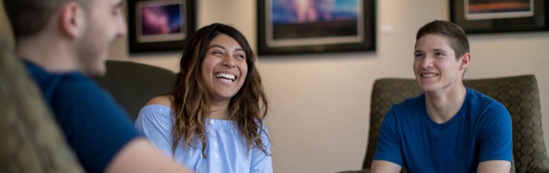 A group of MBA students sit in a lobby while having a friendly conversation.