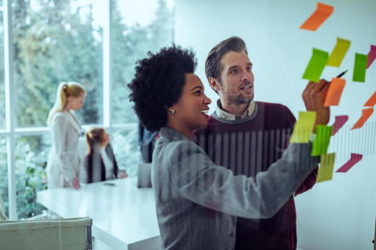 Man and woman placing sticky notes on a glass window