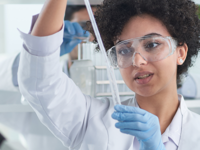 Three scientists in lab coats, gloves and protective glasses work with liquids in test tubes.