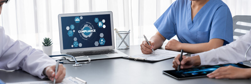 Health care professionals seated at a table, taking notes in front of a "compliance" screen.