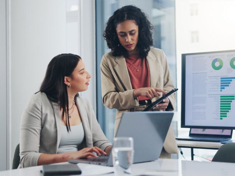 women collaborating in office with graph presentation displaying in the background