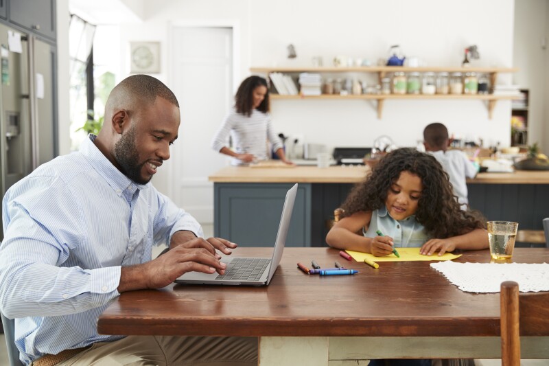 Parent sits at table with daughter on laptop