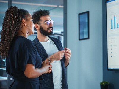 Two marketing professionals, a man and a woman, examine data projected on a screen.