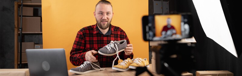 Young bearded vlogger looking at camera reviewing shoes.