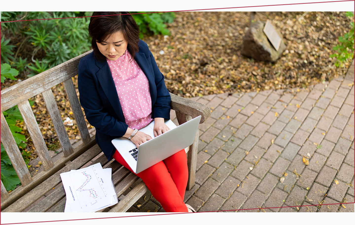 Woman sitting on a wooden bench outdoors using a laptop.