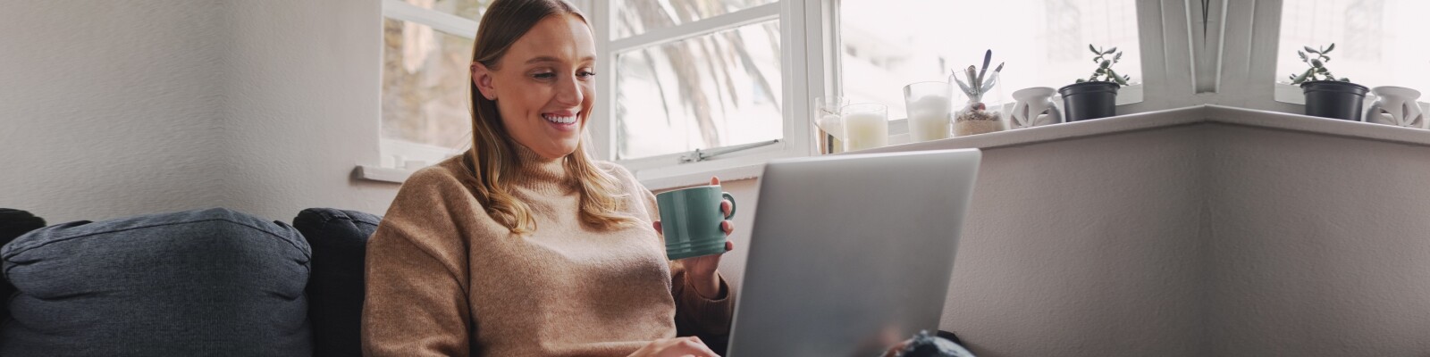 Woman sits on her sofa with a coffee cup working on laptop