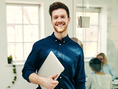 Smiling young businessman standing with his laptop in an office