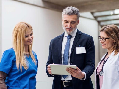 A professional in a suit shows a doctor and a nurse information on a tablet.