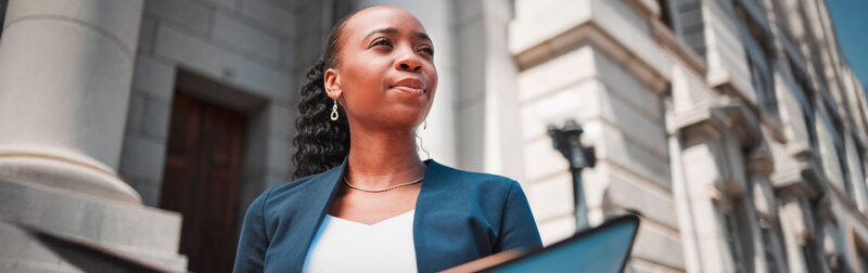 Female lawyer standing outside a law firm looking empowered.