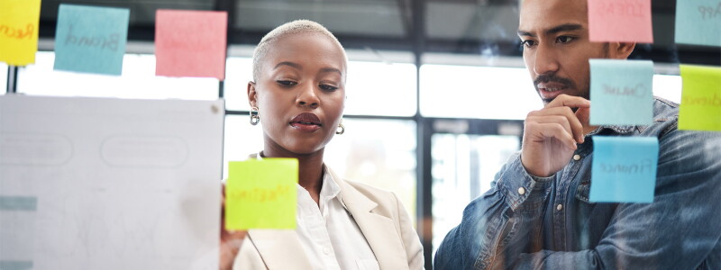 Man and woman looking at ideas on sticky notes at workplace.