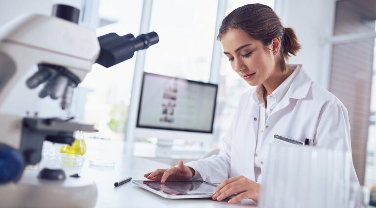 Female researcher in front of microscope reading a tablet