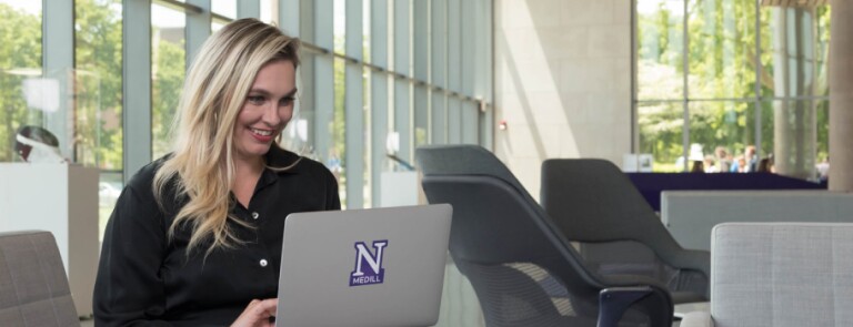 IMC graduate on laptop in the lobby of the Evanston campus