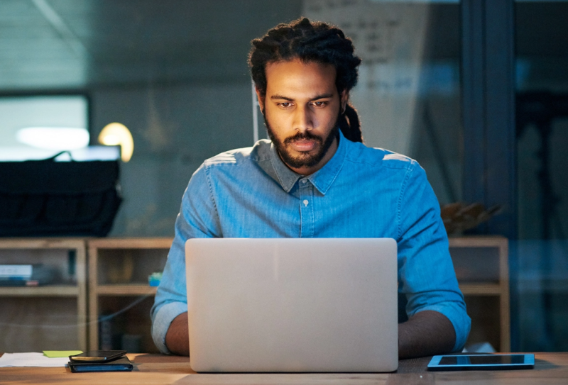 Man in office with blue shirt working on laptop computer