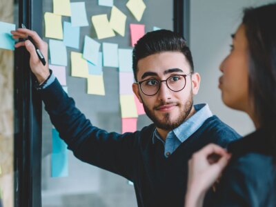Entrepreneur leads multicultural creative employees collaborating on creating presentation using little sticky papers for writing ideas and productive job.