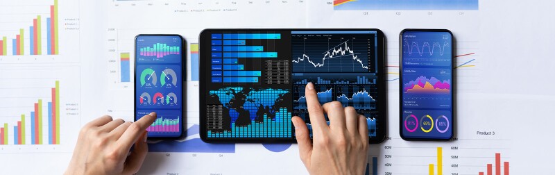 A person's hands working on multiple phone and tablet screens, which rest on bar-graph documents