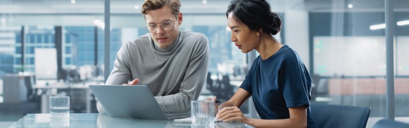 Two people sitting at a table looking at a laptop.