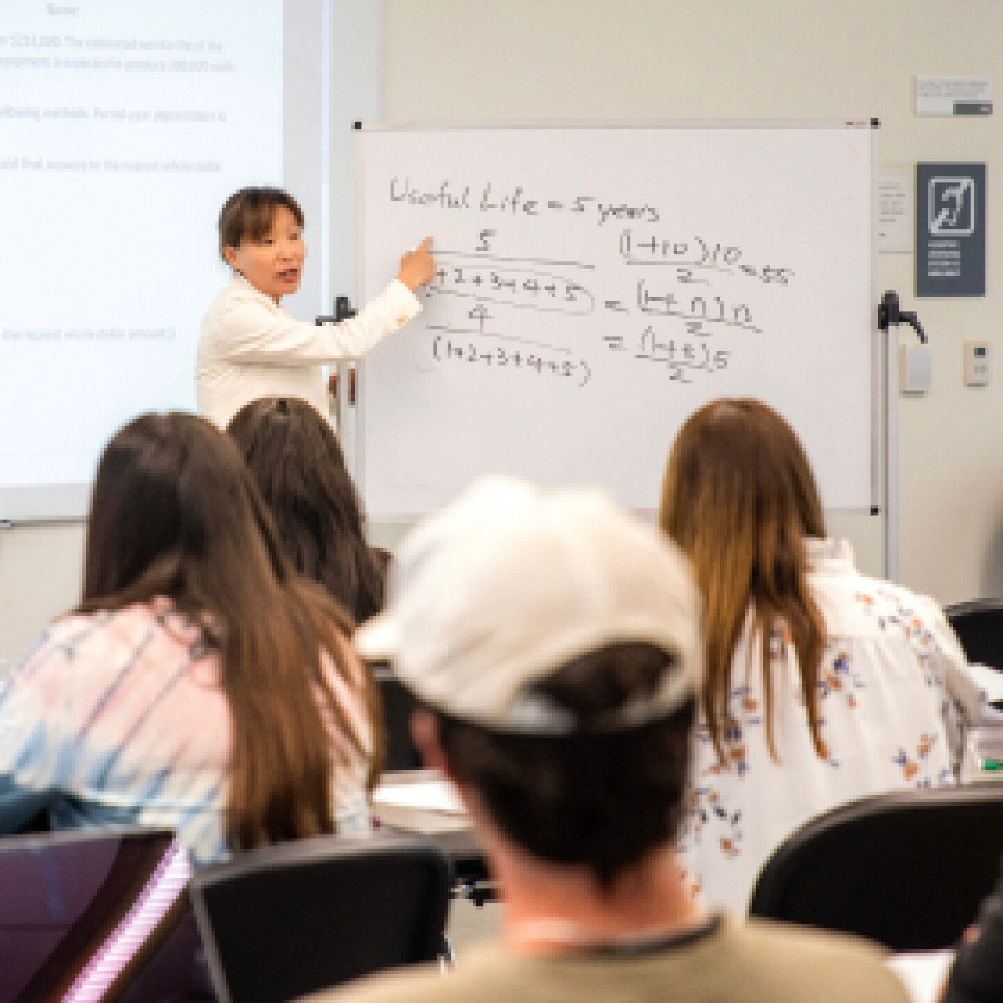 A female CSUMB professor points to whiteboard while teaching classroom of students.