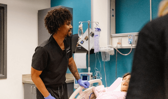 Male nurse in black scrubs working with a medical dummy in a a hospital bed
