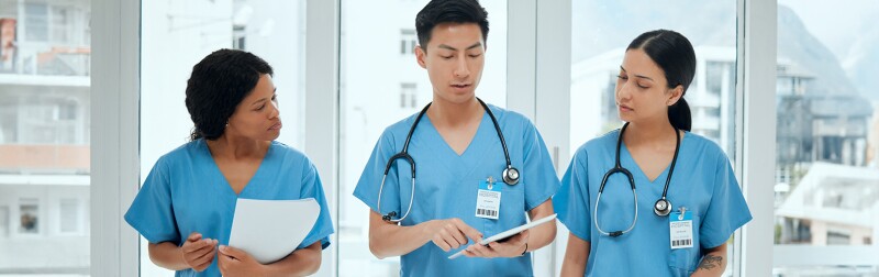 Three nurses discussing patient information, with one using a tablet to explain details.