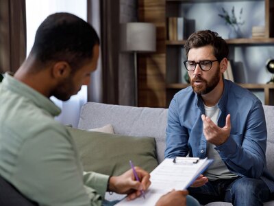 male therapist takes notes on a clipboard while in session with client