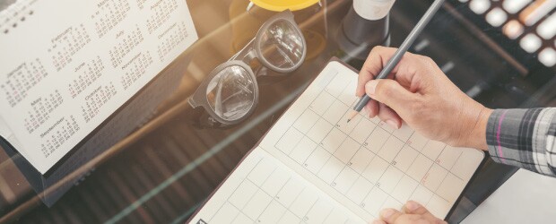 person writing in planner with calendar and glasses in front of them