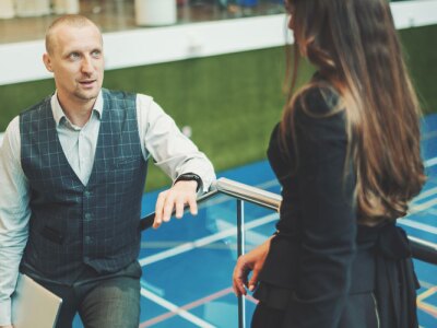 Male sports scout discusses recent scouting trip findings with female director in an indoor court.