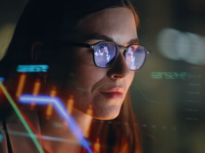 A woman in glasses reviews financial figures reflected on a transparent screen.