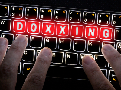 Hands are poised over the keys of a glowing keyboard. The word "doxxing" is highlighted on glowing red keys.