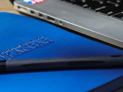A close-up of a pen on a branded KU journal sitting next to a laptop.