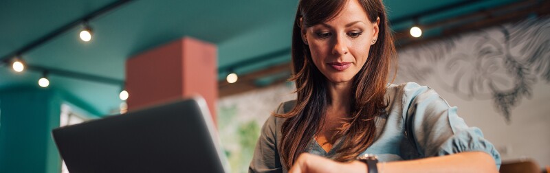Woman checking time on wristwatch while working on her laptop in the cafe.