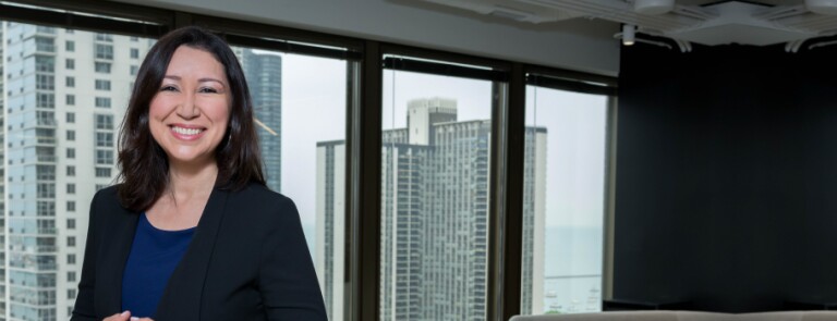 IMC alumni stands in office space while wearing a black blazer