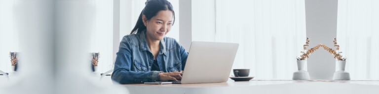 Adult in jean shirt works on laptop at kitchen table