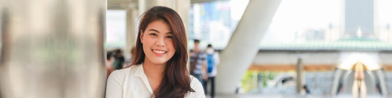 Smiling woman stands on a bridge underneath a highrise building