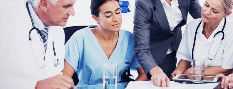 Group of medical professionals seated around table listening to healthcare compliance worker