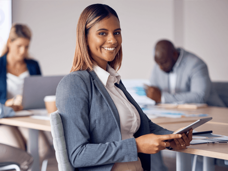 Woman in blazer holding tablet in a room with two colleagues
