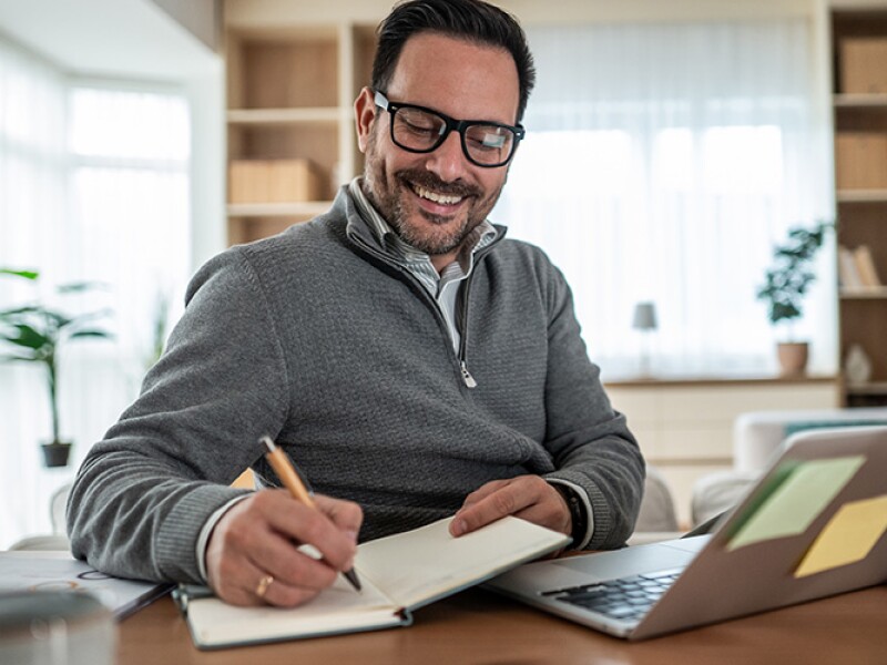 Man writing notes while working on his laptop from home