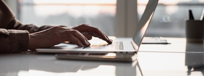 A closeup of the hands of someone working at their desk on a laptop