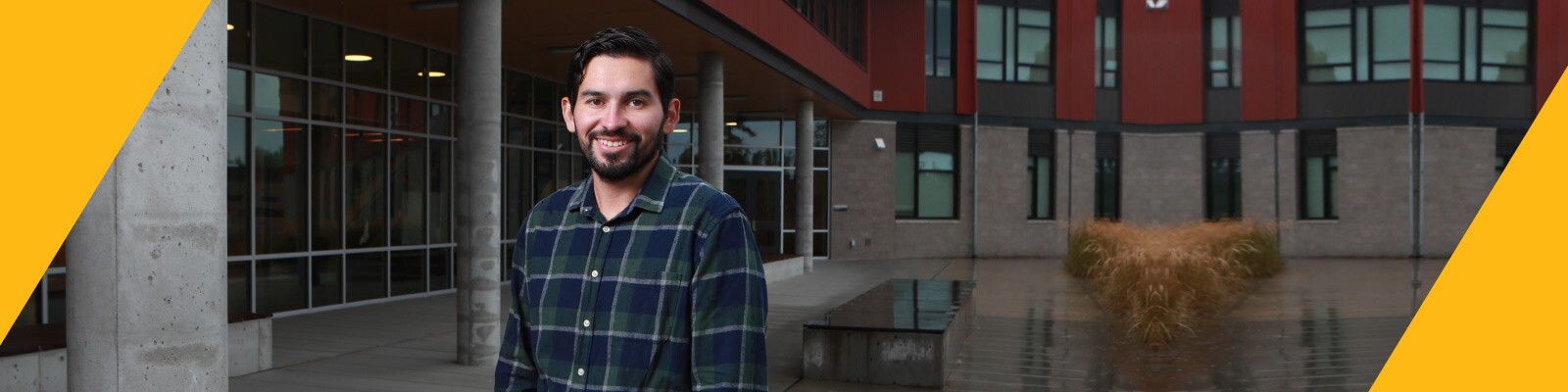 Man wearing plaid button down stands outside in front of a building