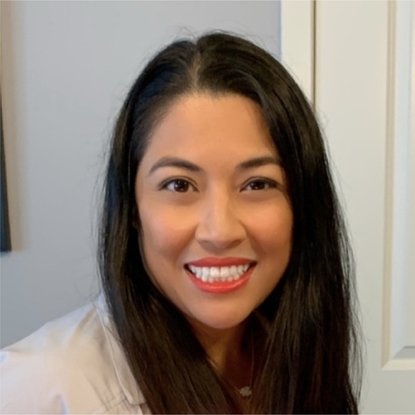 Headshot of Catherine Castillo with long dark hair and red lipstick, wearing a light top, facing camera against a neutral indoor background.