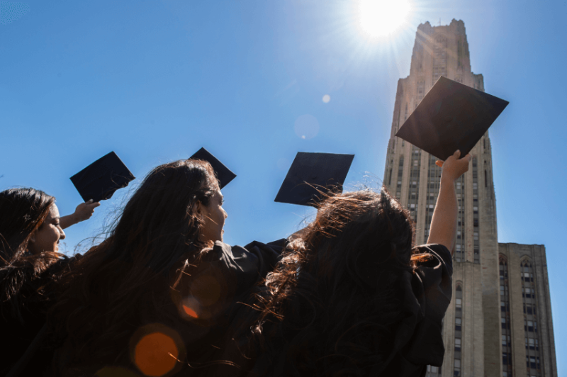 Group of graduates tossing caps outside in front of tall building