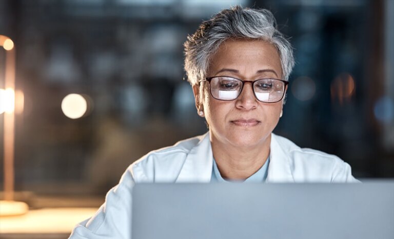 Woman with glasses and lab coat working over laptop computer