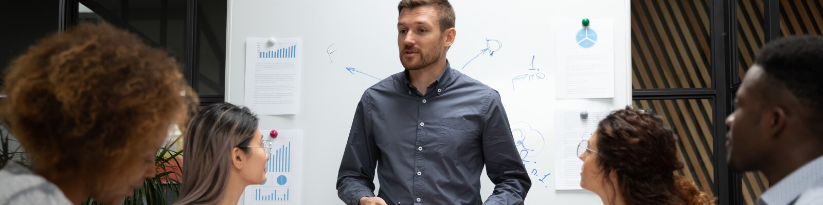 Man leads a team meeting standing in front of a white boar