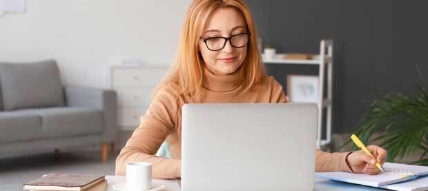 Graduate student taking notes while seated at. laptop
